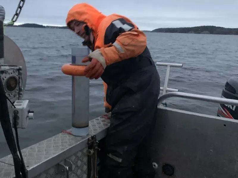 Person i orange flytoverall håller ett upprättstående rör med en orange flytring på båtens reling