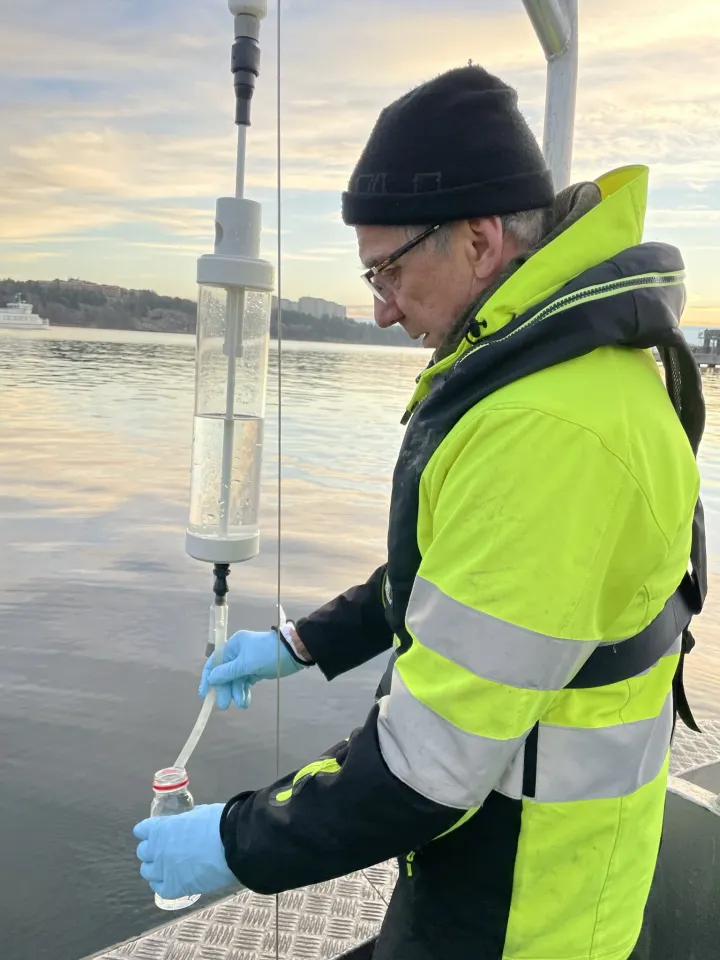 Provtagare i varseljacka tappar vatten från en vattenhämtare till en flaska